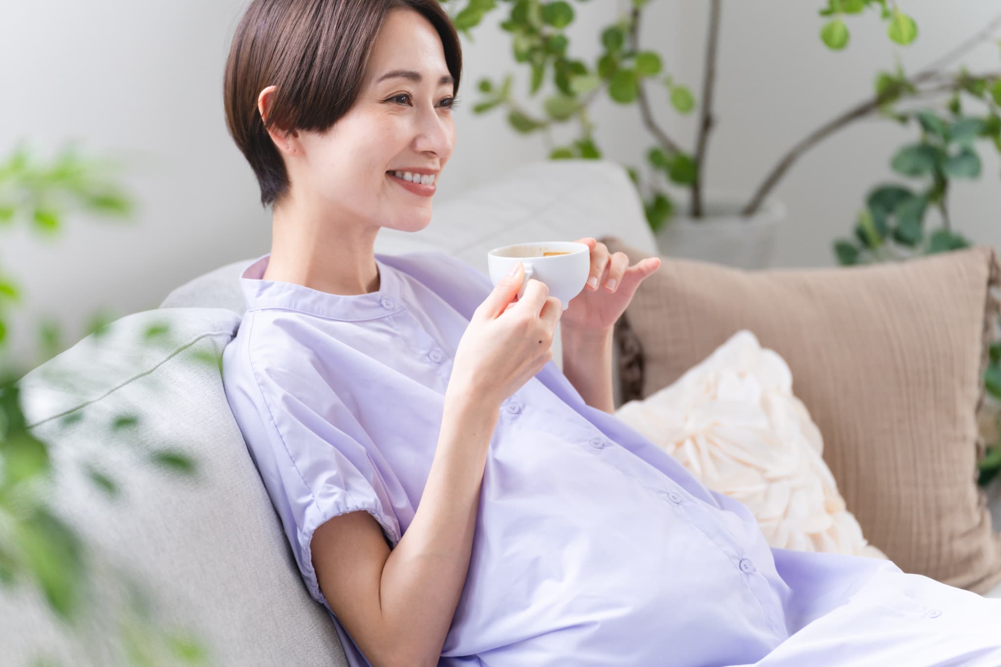 妊娠中の女性がソファで飲み物を飲んでいるイメージ